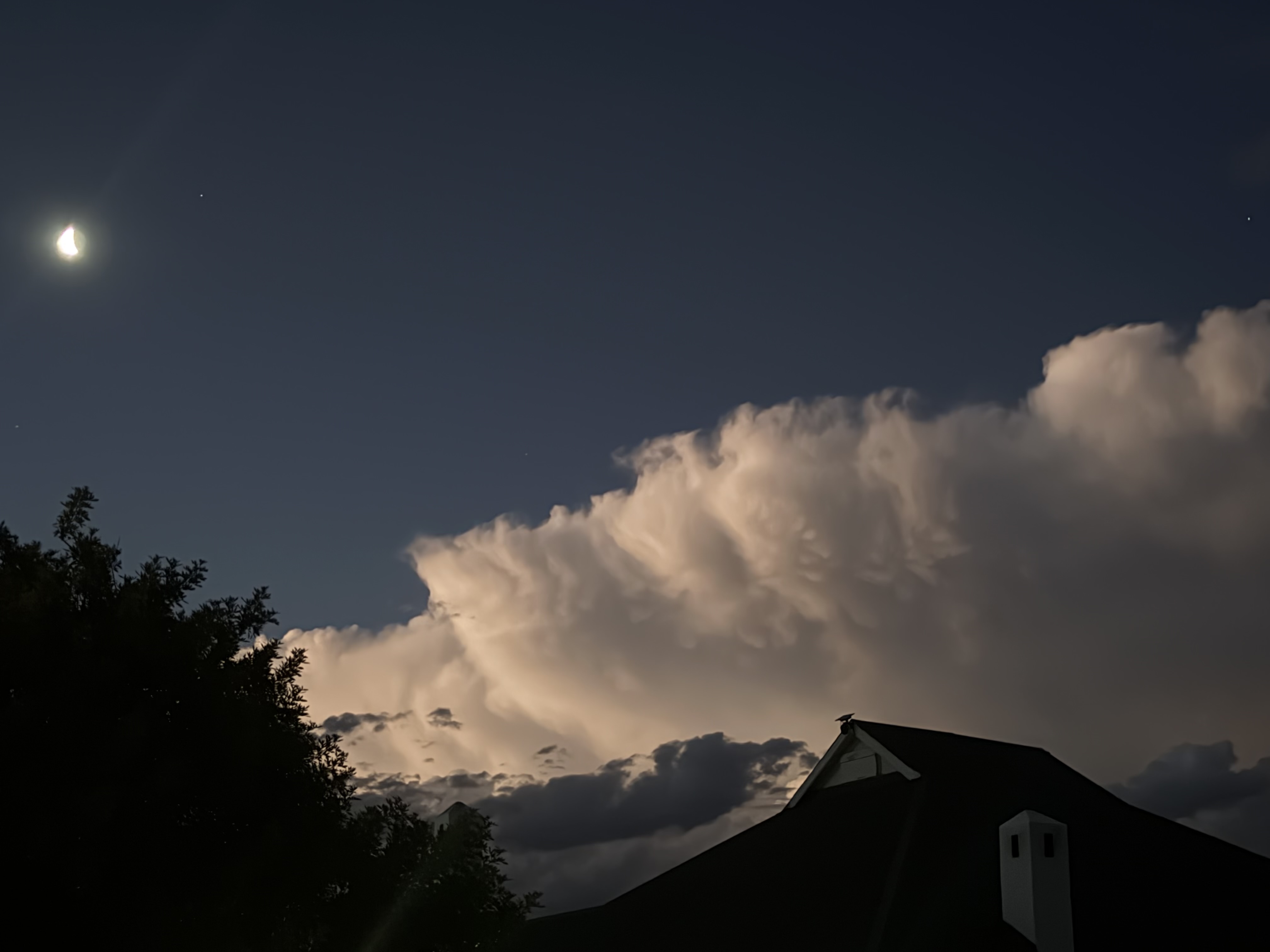 Moon above a towering illuminated cloud at night